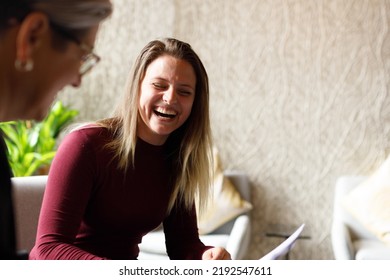 Young Cheerful Caucasian Businesswoman Laughing While Discussing With Mature Female Professional In Meeting At Corporate Office