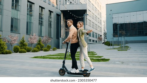 Young cheerful caucasian couple having fun riding electric scooter in sunny weather in the city park near modern office building. Lifestyle. Outside - Powered by Shutterstock