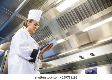 Young cheerful chef using tablet standing in professional kitchen