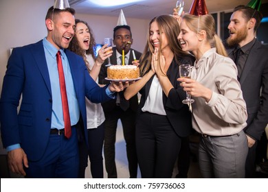 Young Cheerful Company Workers Celebrating Birthday Of Colleague With Cake And Champagne In Office