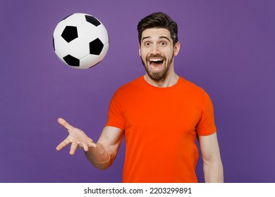 Young Cheerful Cool Surprised Excited Satisfied Fun Fan Man Wears Orange T-shirt Cheer Up Support Football Sport Team Watch Tv Live Stream Toss Up Soccer Ball 2024 Isolated On Plain Purple Background