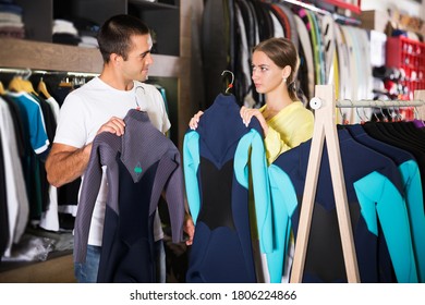 Young Cheerful Couple Choosing Diving Suit In Clothing Store