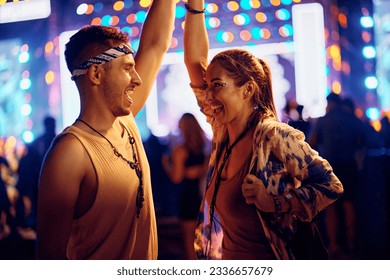 Young cheerful couple dancing while enjoying in summer music festival at night.