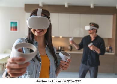 Young cheerful couple guy and girl while playing in virtual reality goggles with controllers in hands at home in apartment. - Powered by Shutterstock