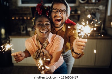 Young cheerful couple having fun with sparklers on New Year's eve at home. 