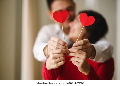 Young cheerful couple in love holding red hearts over eyes and smiling. Happy lovers huging  and enjoy each other. Valentines day celebration concept. Relationship, surprise concept.