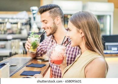 Young Cheerful Couple Toasting Cocktails In Miami Lounge Disco Bar - Young People Having Fun With New Mixology Club Alcohol Beverage - Party And Happy Hour Concept - Focus On Woman Mouth - Warm Filter