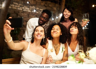 Young Cheerful Friends Communicating In Video Chat Or Taking Selfie By Festive Table While Enjoying Wedding Party In Restaurant