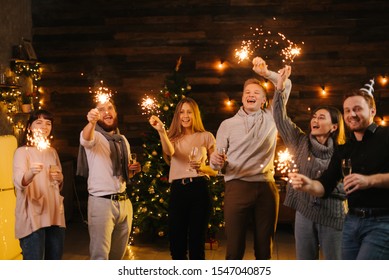 Young cheerful friends dance with Bengali lights, have fun and carefree time celebrating New Year. People dancing with sparklers on dark room and clinking with champagne glasses. - Powered by Shutterstock