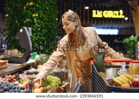 Young cheerful fun customer woman wear casual clothes shopping with trolley cart at supermaket store grocery shop buying choose fruit products inside hypermarket. Purchasing food gastronomy concept