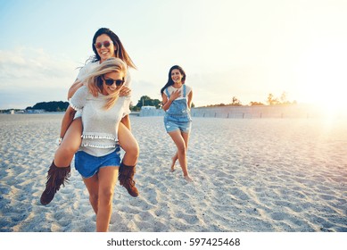 Young cheerful girl giving her friend piggyback ride while third girl laughing at them.  - Powered by Shutterstock