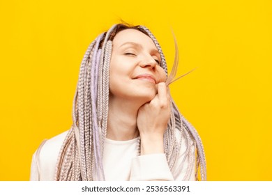 young cheerful girl with gray dreadlocks touches the soft ends of her hair and smiles on a yellow isolated background, woman with an unusual hairstyle and pigtails - Powered by Shutterstock