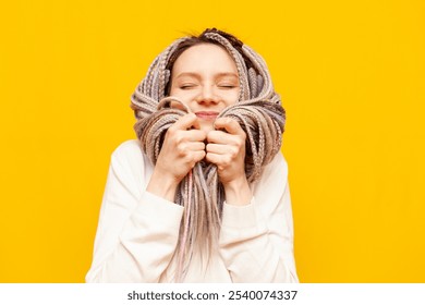 young cheerful girl with gray dreadlocks touches the soft ends of her hair and smiles on a yellow isolated background, woman with an unusual hairstyle and pigtails - Powered by Shutterstock