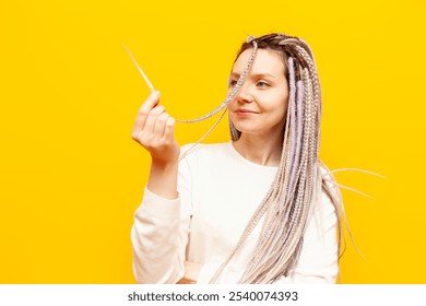 young cheerful girl with gray dreadlocks touches the soft ends of her hair and smiles on a yellow isolated background, woman with an unusual hairstyle and pigtails - Powered by Shutterstock