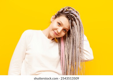 young cheerful girl with gray dreadlocks touches the soft ends of her hair and smiles on a yellow isolated background, woman with an unusual hairstyle and pigtails - Powered by Shutterstock