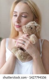 Young cheerful girl in nightie hugs toy bear.