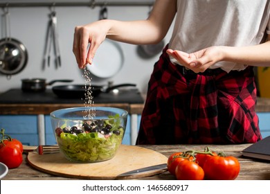 young cheerful girl prepares a vegetarian salad in the kitchen, she salts and adds spices, the process of preparing healthy food