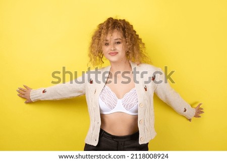 Young cheerful girl smiling at the camera while standing on a yellow background close-up.