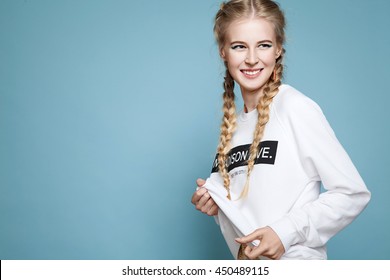 Young Cheerful Girl In A White Sweatshirt With Braids On A Blue Background