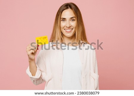 Young cheerful happy fun woman she wear shirt white t-shirt casual clothes hold in hand mock up of credit bank card isolated on plain pastel light pink background studio portrait. Lifestyle concept