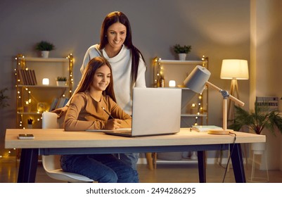 Young cheerful happy mother with her teen school girl daughter studying online class on laptop at home during remote lesson. Woman parent helping child with homework. Distance education. - Powered by Shutterstock