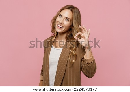 Young cheerful happy smiling fun successful employee business woman 30s she wearing casual brown classic jacket showing okay ok gesture isolated on plain pastel light pink background studio portrait
