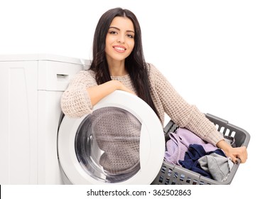 Young Cheerful Housewife Holding A Laundry Basket And Posing Next To A Washing Machine Isolated On White Background
