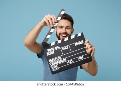 Young cheerful man in casual clothes posing isolated on blue wall background, studio portrait. People lifestyle concept. Mock up copy space. Holding in hands classic black film making clapperboard - Powered by Shutterstock