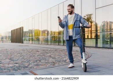 Young cheerful man with e-scooter using scooter-sharing system application on his smartphone