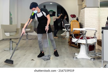 Young Cheerful Man Hairdresser In Mask Cleaning Floor In The Beauty Salon