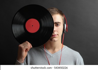 Young Cheerful Man Listening To Music On Headphones And Holds The Vinyl In Hand, On A Black Background.