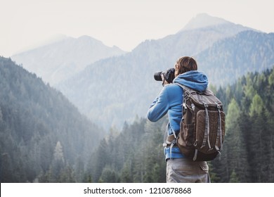Young cheerful man photographer taking photographs with digital camera in a mountains. Travel and active lifestyle concept