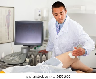 Young cheerful  man sonographer using ultrasonography machine checking female patient in hospital diagnostic room
