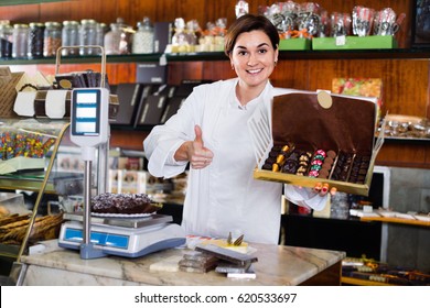 Young cheerful positive female seller offering large box of chocolates in confectionery - Shutterstock ID 620533697