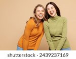 Young cheerful positive happy friends two women they wears orange green shirt casual clothes together laugh joking isolated on plain pastel light beige background studio portrait. Lifestyle concept