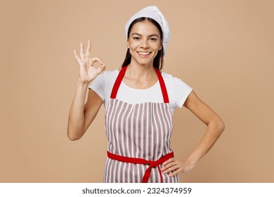 Young cheerful smiling fun housewife housekeeper chef cook baker latin woman wear striped apron toque hat show ok okay stand akimbo isolated on plain pastel light beige background Cooking food concept - Powered by Shutterstock