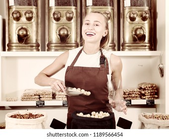 Young cheerful  smiling woman is offering nuts and on the plate is written Macadamia in Catalan in the store. - Shutterstock ID 1189566454