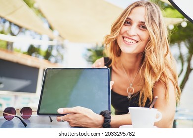 Young Cheerful Spanish Woman Showing Tablet To Camera In Cafeteria