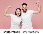 Young cheerful strong sporty fitness couple two friends man woman 20s in white basic blank print design t-shirts showing biceps muscles on hand isolated on pastel pink color background studio portrait