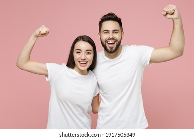 Young cheerful strong sporty fitness couple two friends man woman 20s in white basic blank print design t-shirts showing biceps muscles on hand isolated on pastel pink color background studio portrait - Shutterstock ID 1917505349