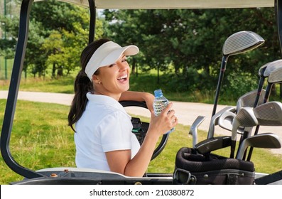Young cheerful woman with bottle of water driving golf cart 