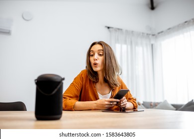 Young Cheerful Woman Controlling Home Devices With A Voice Commands, Talking To A Smart Column At Home. Concept Of Smart Home And Voice Command Control