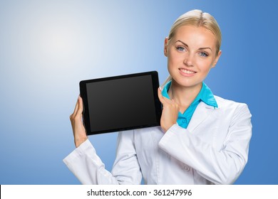 Young cheerful woman doctor is showing her blank tablet