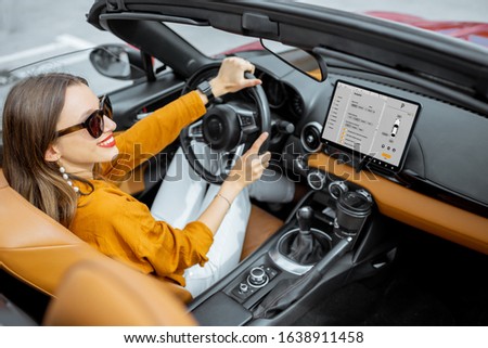 Young and cheerful woman driving sports car with a digital touchscreen with launched controlling program on the front dashboard