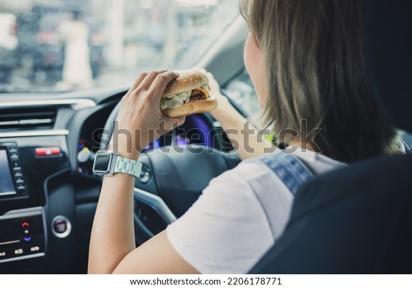 Young and cheerful woman\
eating healthy sandwich with salad homemade while driving car in\
the city.