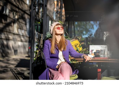 Young Cheerful Woman In Purple Coat Sitting In Street Cafe Enjoying Sunny Spring Day