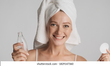 Young Cheerful Woman With Towel On Head Holding Cotton Sponge And Face Tonic Happily Looking In Camera Isolated On White Background