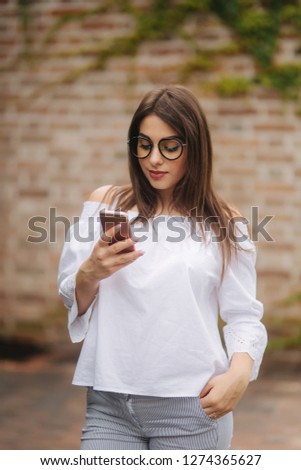 Young cheerful woman watching funny video on smart phone while resting outdoors