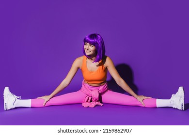 Young Cheerful Woman Wearing Colorful Sportswear Doing Splits Against Purple Background