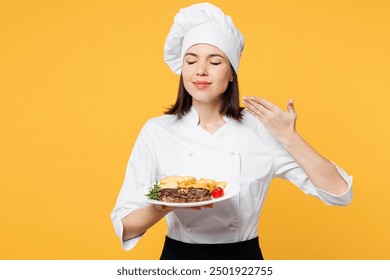 Young chef baker woman wear white shirt black apron uniform toque chefs hat hold plate ready order dish steak, raise hand to face, feel food smell isolated on plain yellow background Cook food concept - Powered by Shutterstock